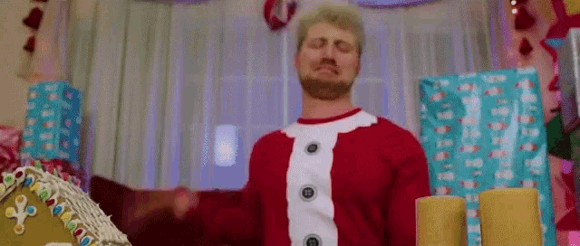a man in a santa claus sweater is standing next to a gingerbread house .