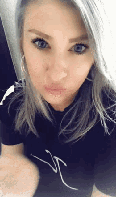 a woman with gray hair and blue eyes is wearing a black shirt with the letter j on it .
