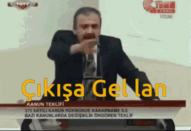 a man in a suit and tie is giving a speech in front of a screen that says ' çikisa gel lan '