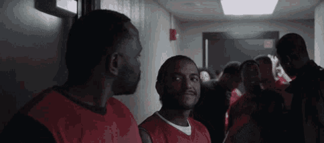 a group of men in red jerseys are standing in a hallway talking to each other .