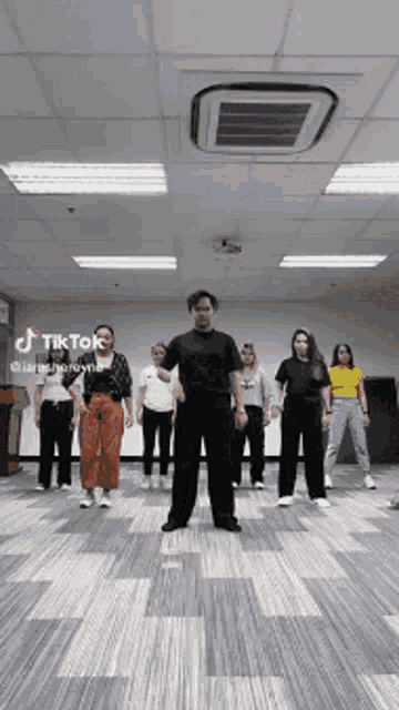 a group of people are dancing in a room with tik tok written on the bottom of the screen
