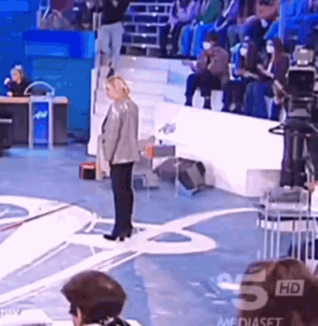 a woman is standing on a stage in front of a crowd and a sign that says mediaset 5 hd