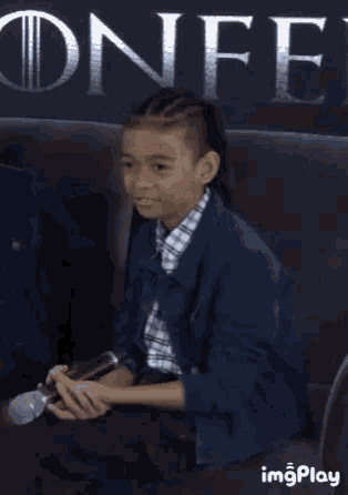 a young boy sits on a couch holding a microphone in front of a sign that says onfe