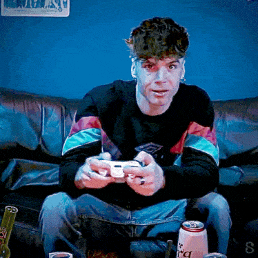 a man is sitting on a couch playing a video game while a can of soda sits next to him