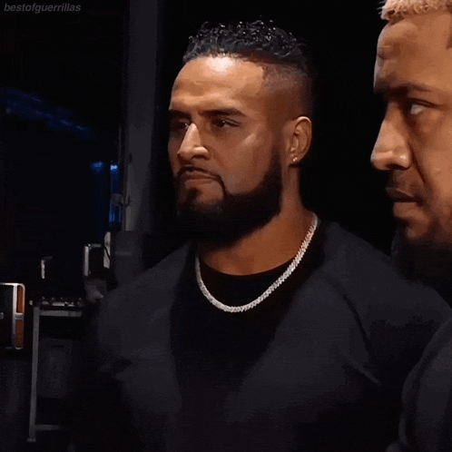 a man with a beard wearing a diamond chain looks at another man