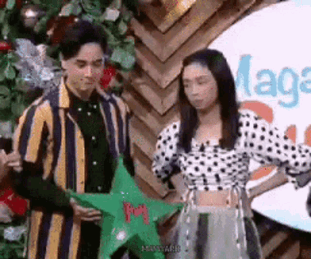 a man and a woman are standing next to each other and holding a green star .