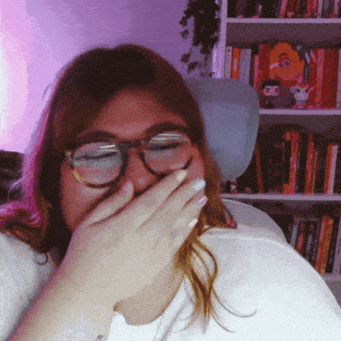 a woman wearing glasses is covering her mouth with her hands