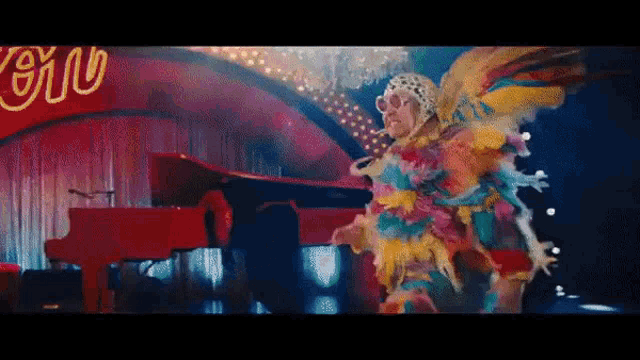 a man in a colorful outfit is playing a red piano