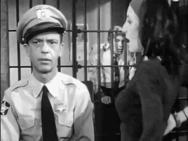 a black and white photo of a police officer and a woman standing in front of a jail cell .