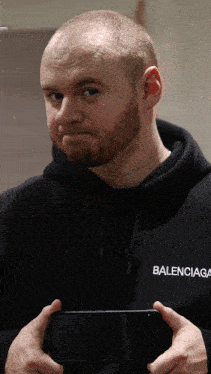 a man wearing a balenciaga sweatshirt holds a cell phone