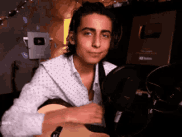 a young man is holding a guitar in front of a microphone .