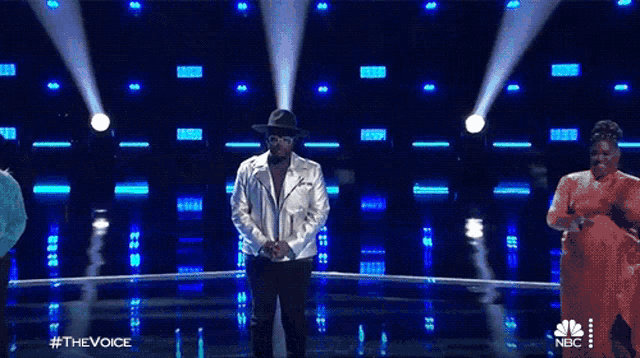 a man wearing a hat and glasses is on a stage with his hands folded in prayer ..