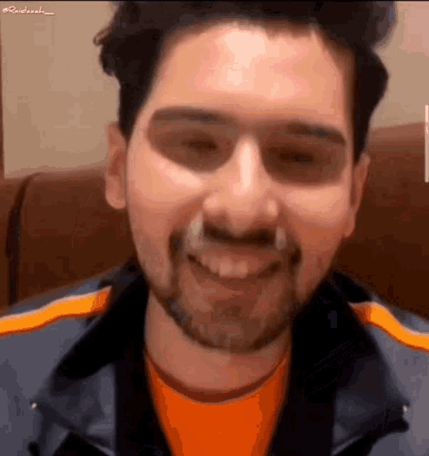 a man with a beard is smiling while wearing an orange shirt