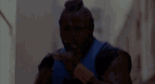 a man in a blue shirt is standing in a dark room with his hands on his face .