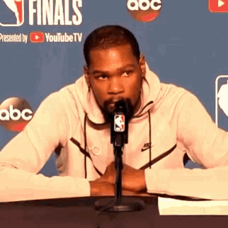 a man is sitting at a table in front of a microphone with a nba logo on it .