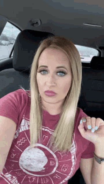 a woman in a red shirt with a zodiac sign on it is sitting in a car