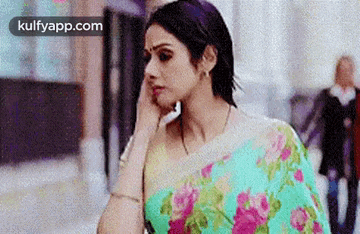 a woman is talking on a cell phone while wearing a floral saree .