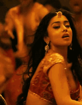 a woman in a red top and gold earrings is dancing in front of a crowd .