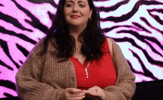 a woman wearing a brown cardigan and a red top stands in front of a zebra print background