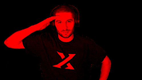 a man wearing headphones and a black shirt with a yellow x on the front salutes