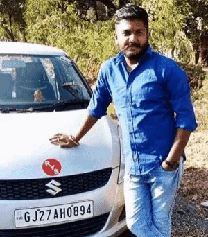 a man in a blue shirt stands next to a white suzuki car