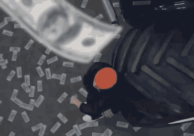 a man in a black hoodie is laying on the ground with money falling around him and a tractor tire in the background