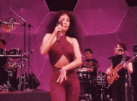a woman in a red dress is dancing on a stage with a band behind her .