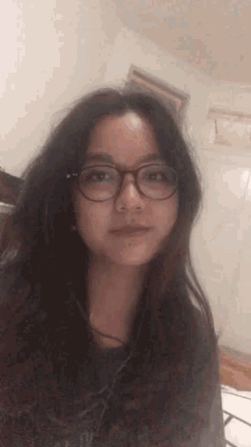 a young woman wearing glasses is taking a selfie in a room .