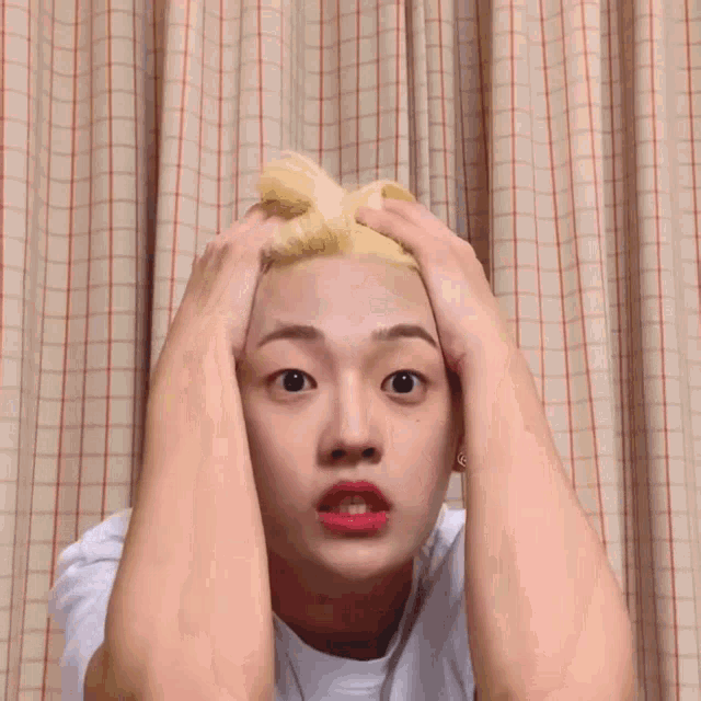 a young man with blonde hair and red lips is making a funny face with his hands in the air .