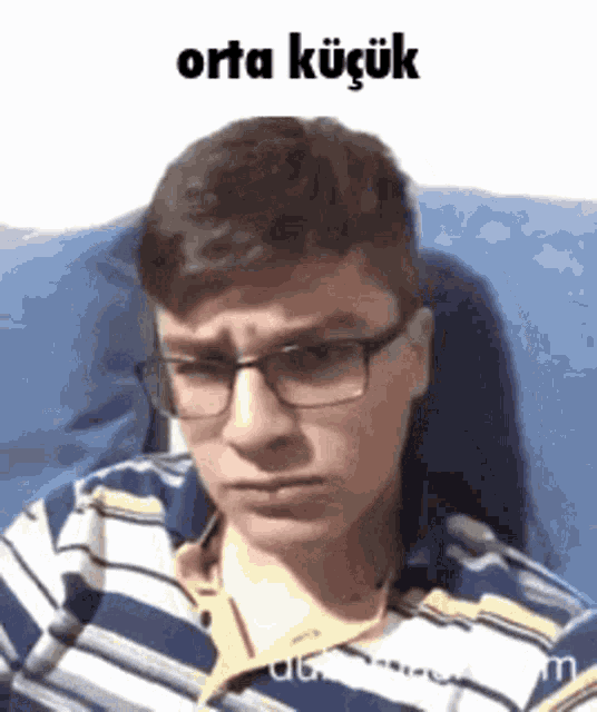 a man wearing glasses and a striped shirt is sitting on a couch .