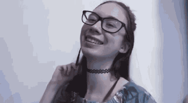 a young girl wearing glasses and a choker is smiling and looking at the camera .