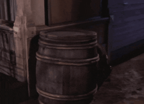 a man in a cowboy hat is behind a wooden barrel