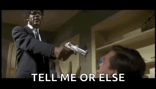 a man in a suit and tie is pointing a gun at another man and says `` tell me or else '' .