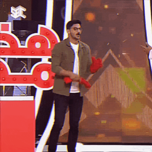 a man wearing glasses and a green jacket is standing on a stage holding a pair of red gloves ..