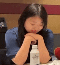 a woman is sitting at a table with her eyes closed and a bottle of unifort in front of her .