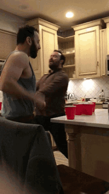 two men are dancing in a kitchen with red cups on the countertop