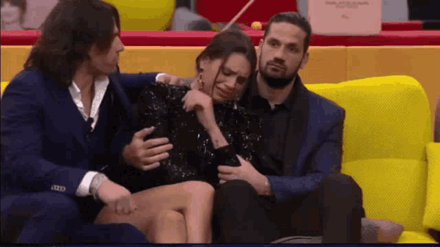 three people are sitting on a yellow couch and one of them is holding a woman 's leg