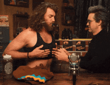 two men are sitting at a table with a sign that says 24