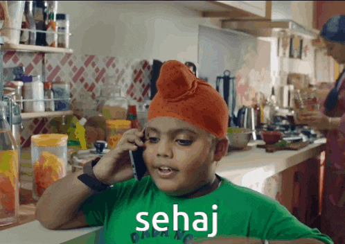 a boy wearing an orange turban is talking on a cell phone and the word sehaj is on the bottom