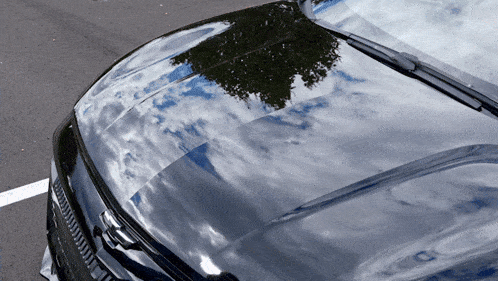 the hood of a black car is reflecting the sky