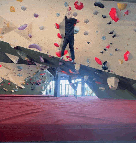 a person climbs a climbing wall with a red mat