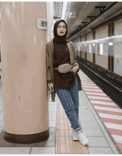 a woman wearing a hijab is leaning against a pillar at a subway station
