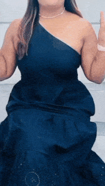 a woman in a black one shoulder dress is kneeling down and waving her hand .