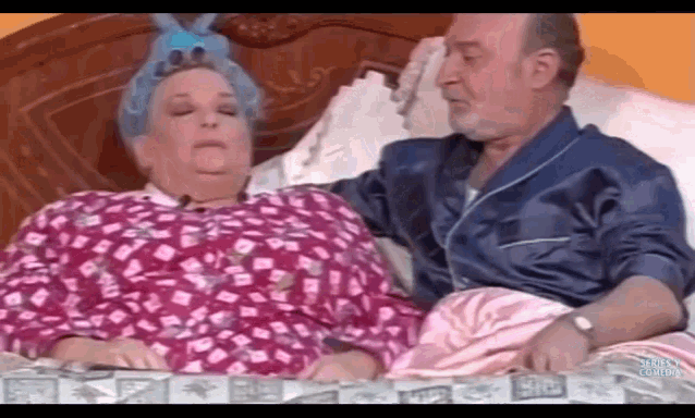 a man and a woman are laying on a bed and the woman has a blue bunny on her head
