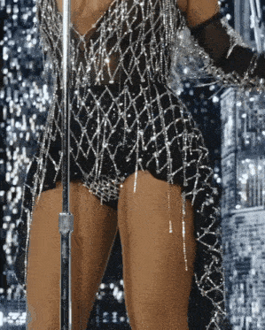 a woman singing into a microphone wearing a black and silver outfit