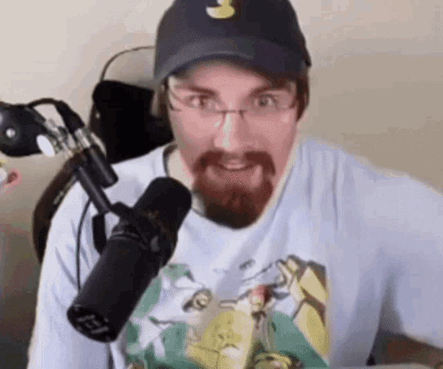 a man with a beard wearing a hat and glasses is standing in front of a microphone ..
