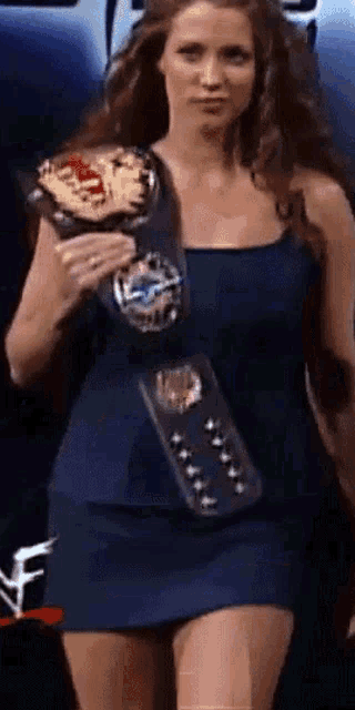 a woman in a blue dress is holding a wrestling championship belt around her waist .