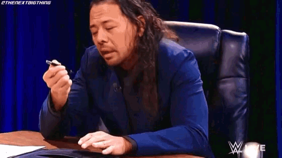 a man in a blue suit is sitting at a table with his eyes closed and holding a pen .