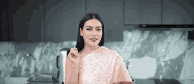 a woman in a pink dress is standing in a kitchen looking at the camera
