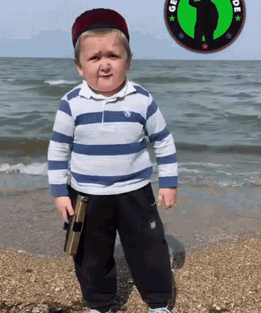 a young boy standing on a beach holding a book and wearing a striped shirt with the letter e on the front